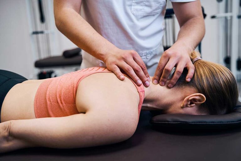 A chiropractor gently palpating the mid-back of an adult patient in a bright clinic setting.