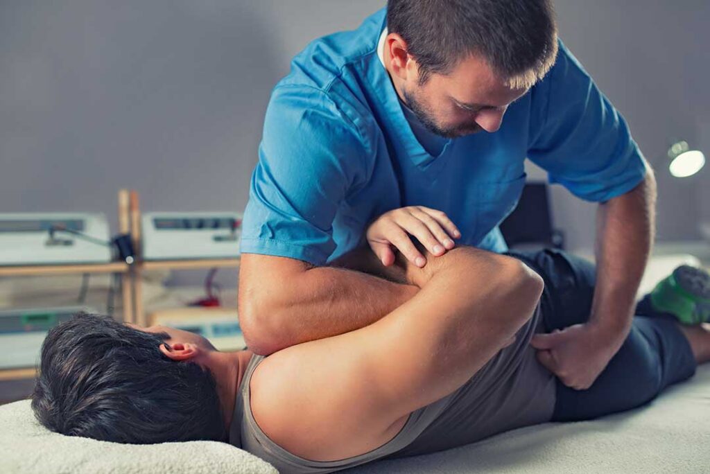 Two adults talking at home while one points to their lower back, discussing discomfort and possible causes.